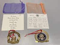 Two White House Christmas ornaments with accompanying brochures and storage bags on a neutral surface.