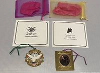 Two White House Christmas ornaments displayed with their brochures and colored organza storage bags