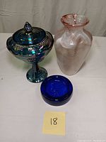 Full lot photo showing carnivale glass compote with lid on the left, art glass vase in center, and cobalt blue rooster dish in front.
