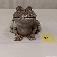 Front view of the large cement garden frog sculpture showing facial features and weathered paint.