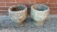 Front view of the two cement planters showing textured decorative designs and weathered condition.