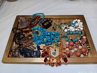 Top-down image of assorted costume jewelry and decorative items on wooden tray.
