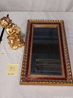 Photo of the golden enameled Cupid figurine sitting next to the ornate wall mirror showing both items in the lot.