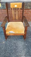 Frontal photo of antique Mission oak rocking chair showing vertical slat back, wooden arms, and torn yellow fabric seat and headrest.