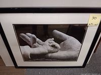Full view of the framed black and white print showing a large adult hand holding a smaller child's hand, with yellow label showing measurements.