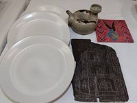 Photo showing three white Bennington pottery dinner dishes, ceramic donut-shaped vessel, engraved New Orleans Lace Balcony slate art, and colorful tile art.