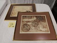 Two framed lithographic prints signed by Priscilla McIver showing abstract figure studies with muted brown and beige tones, photographed on white surface.