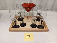Set of six black stemmed glasses and one red art glass martini glass on wooden tray.