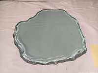 Top view of the irregular-shaped tinted glass slab with sculptured edges on a flat surface.