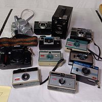 Overview of entire camera lot showing eleven vintage cameras of various makes including Kodak, Nikon, and Gaf