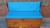 Front view of vintage storage bench showing wooden base with bright blue upholstered padded seat and backrest.