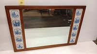 Full view of the large rectangular mirror with wood frame and 10 blue and white scenic Dutch style ceramic tiles inlaid on sides.