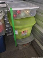 Stack of three plastic storage totes: one transparent with various Christmas balls visible inside, one green, one translucent gray.