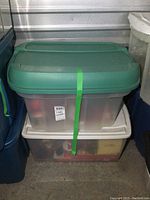 Two plastic storage totes stacked with green and white lids holding Christmas decorations