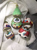 Four small hinged porcelain holiday trinket/music boxes shown open on white tissue