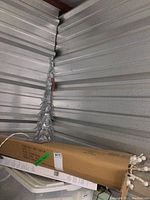 Photo of silver metal decorative Christmas tree with scrollwork design placed in storage unit corner.