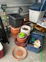 Overall view of stacked plastic and ceramic planters, garden tools including shovel and potato fork, gardening gloves, and storage containers with garden items.