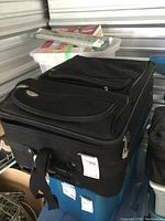 Large black soft-sided suitcase with Samsonite logo patch on front pocket, showing signs of wear