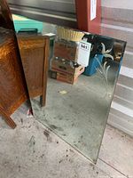 Rectangular beveled mirror angled against a storage wall, showing wear and dirt on the surface and surrounding items reflected.