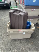 Three large beige plastic storage bins stacked with lids, placed outdoors on gravel ground.