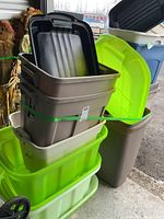Stack of mixed-size plastic storage bins in green, gray, and cream with visible green strap securing them.