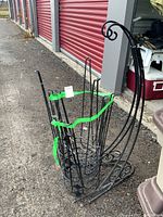 Two metal plant stands and two metal plant hangers banded together. Stands have circular holders and vertical bars. Hangers are tall with a scrolled decorative top, all black metal.