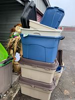 Stack of four large plastic storage bins with lids; three beige bins with brown lids and one blue bin with blue lid on top.