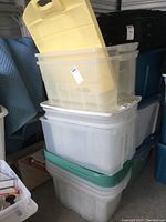 Stack of clear plastic totes with green, white, and yellow lids showing their size and colors