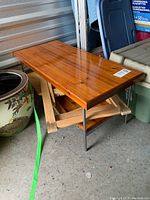 Wood table with a polished wood surface and green metal legs, alongside a folded wood chair and a wood TV tray underneath it.