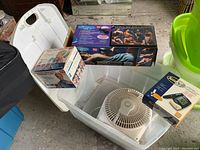 White plastic storage bin containing an electric fan, a boxed muscle toner/massager device, and AccuSync glucose monitoring kit box