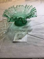 Side view of green depression glass bowl showing ruffled scalloped edge, circular geometric pattern and pedestal base.