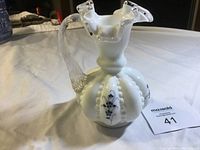 White ornamental jug with scalloped mouth, clear twisted handle, and blue flower hand painted decoration on ribbed body.