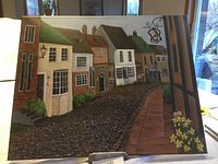 Photo of oil painting showing cobblestone street with row houses and sidewalk with flowers, signed by Carol Sweet, dimensions approximately 16x20 inches.