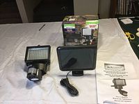 Motion light, solar panel, user manual, and original box on white cloth background.