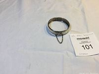 Vintage sterling silver hinged bangle bracelet with safety chain, closed view showing rounded and smooth finish with some decorative patterning.