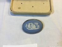 Close-up photo of Wedgwood jasper brooch showing oval shape, blue jasper base and white classical relief figures with twisted rope sterling silver border.