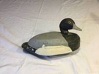 Side view of the bluebill drake decoy showing painted body, yellow and black glass eyes, and crack on neck.
