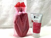 Photo showing the sugar scrub in a mesh gift bag, pink color visible, along with the sugar scrub tube standing beside it.