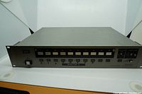 Front angle view of the Panasonic AG-SW100 switcher unit showing rack mount design and input buttons.