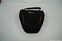 Front view of black Lowepro camera bag with orange accents and handle on top, showing compact shape and logo.