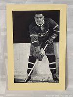 Full photo of Bernard Geoffrion standing in hockey pose with stick, signed at the bottom, surrounded by cream matting.