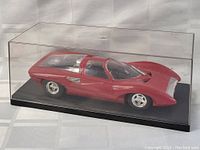 Front right angled view of the red 1960s Barris model car in an acrylic case, showing aerodynamic styling and clear canopy.