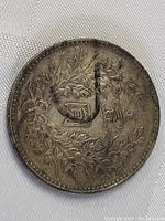 Reverse side of the coin featuring a floral wreath encircling a square character and additional Chinese text.