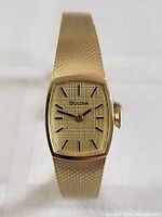 Front view of gold plated vintage Bulova ladies wristwatch showing textured dial, black markers and hands, and gold plated mesh style bracelet.