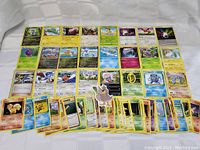 Two images showing 50 different Pokemon trading cards spread on a white cloth background.