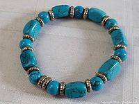 Overall view of the circular expandable turquoise and silver-tone bead bracelet on a white textured background.