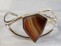 Sterling silver bracelet with a polished triangular agate stone centerpiece, set in a wave designed band, displayed on white cloth background.