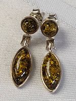 Close-up front view of amber earrings showing round upper and larger marquise lower stones in sterling silver settings.