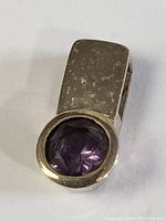 Close-up photo of the chunky sterling silver pendant with round faceted amethyst gemstone, showing hammered texture on the silver and polished bezel setting around the stone.