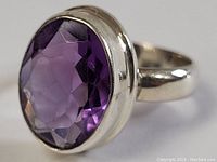 Close-up of oval faceted amethyst stone set in sterling silver bezel ring, highlight of gemstone color and cut.